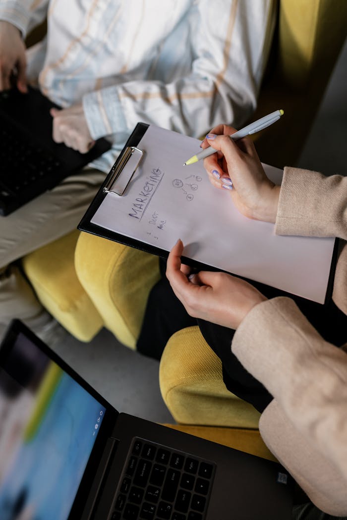 Two professionals in an office working on marketing strategy with laptops and notes.